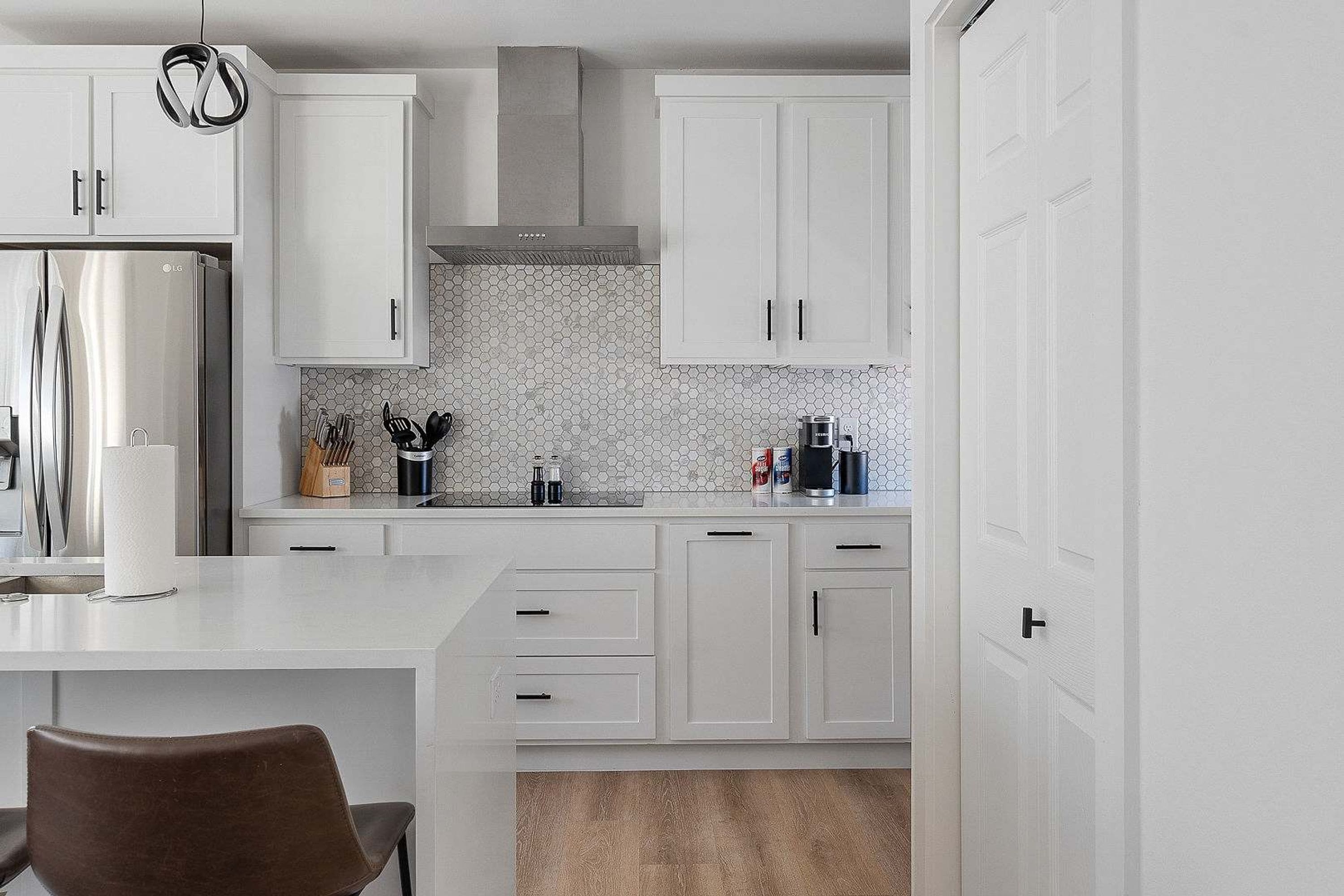 A modern kitchen with white cabinets, a stainless steel refrigerator, and a hexagonal backsplash.