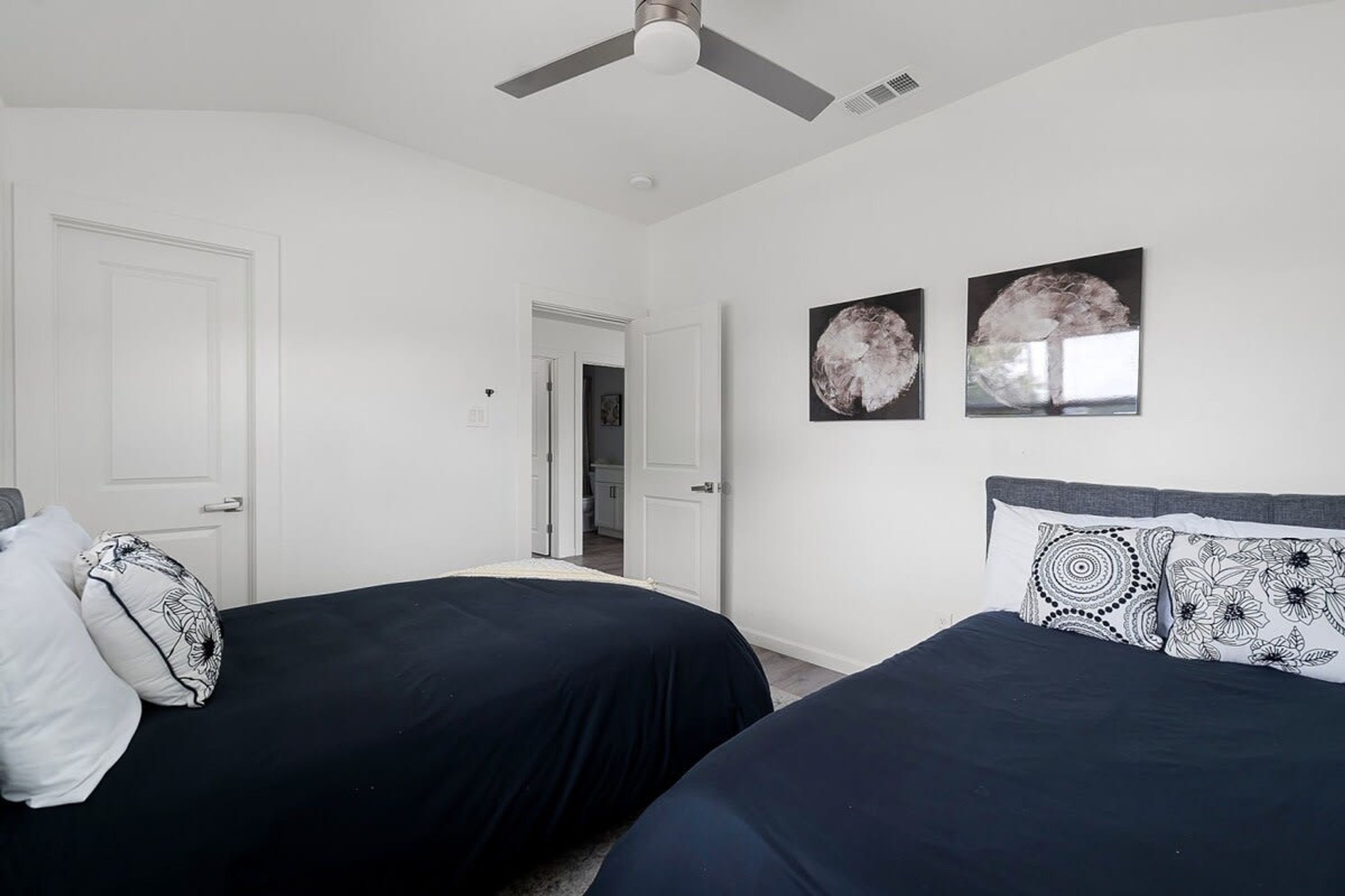 A bedroom with two beds, white walls, and ceiling fans.