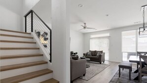 A modern living room with a staircase, a ceiling fan, and a dining area with a table and chairs.