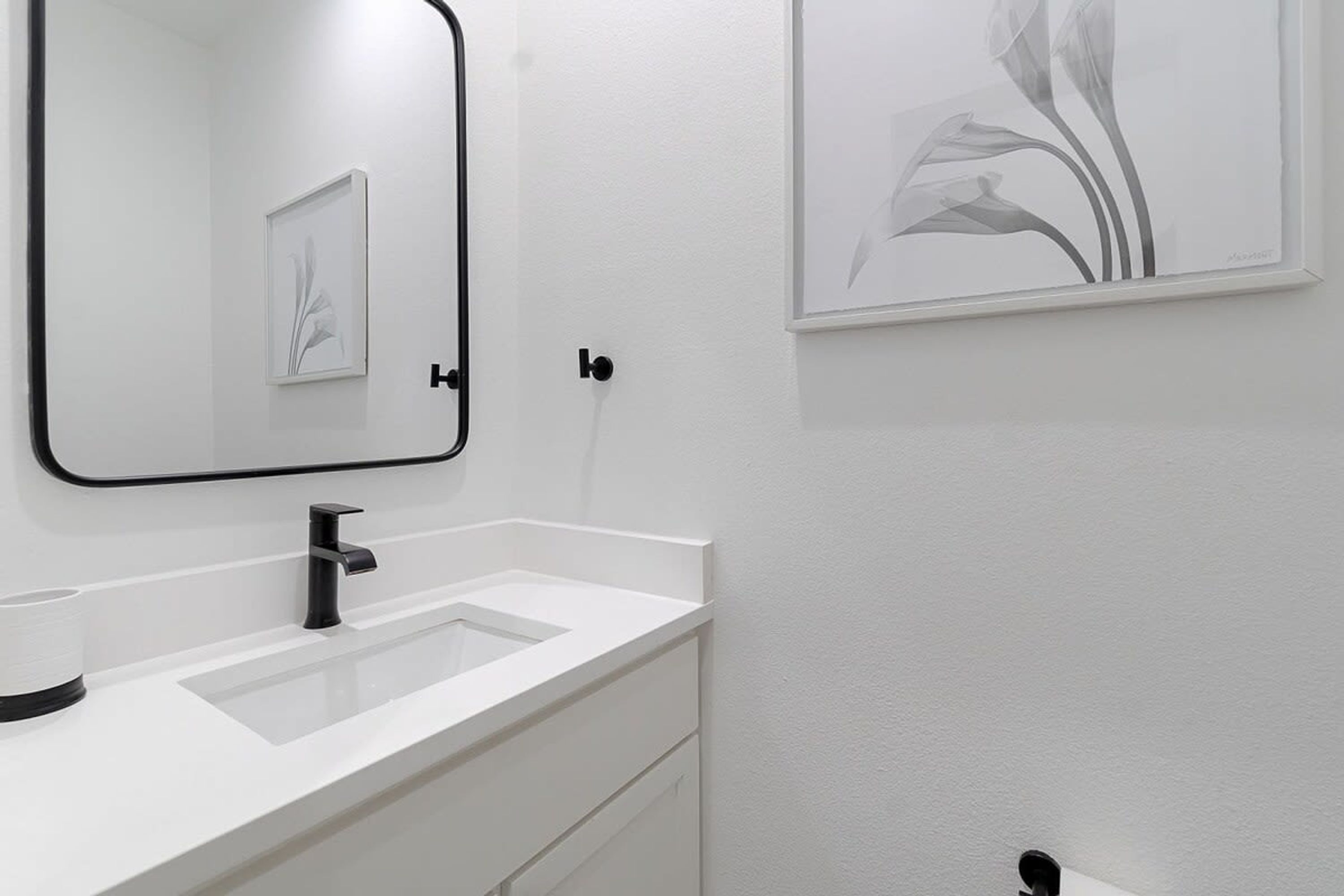 Un baño moderno con un lavamanos blanco, un grifo negro y una obra de arte floral enmarcada en la pared.