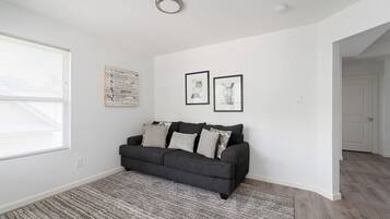 Un salon avec un canapé gris foncé, un tapis à motifs et deux tableaux encadrés accrochés au mur.