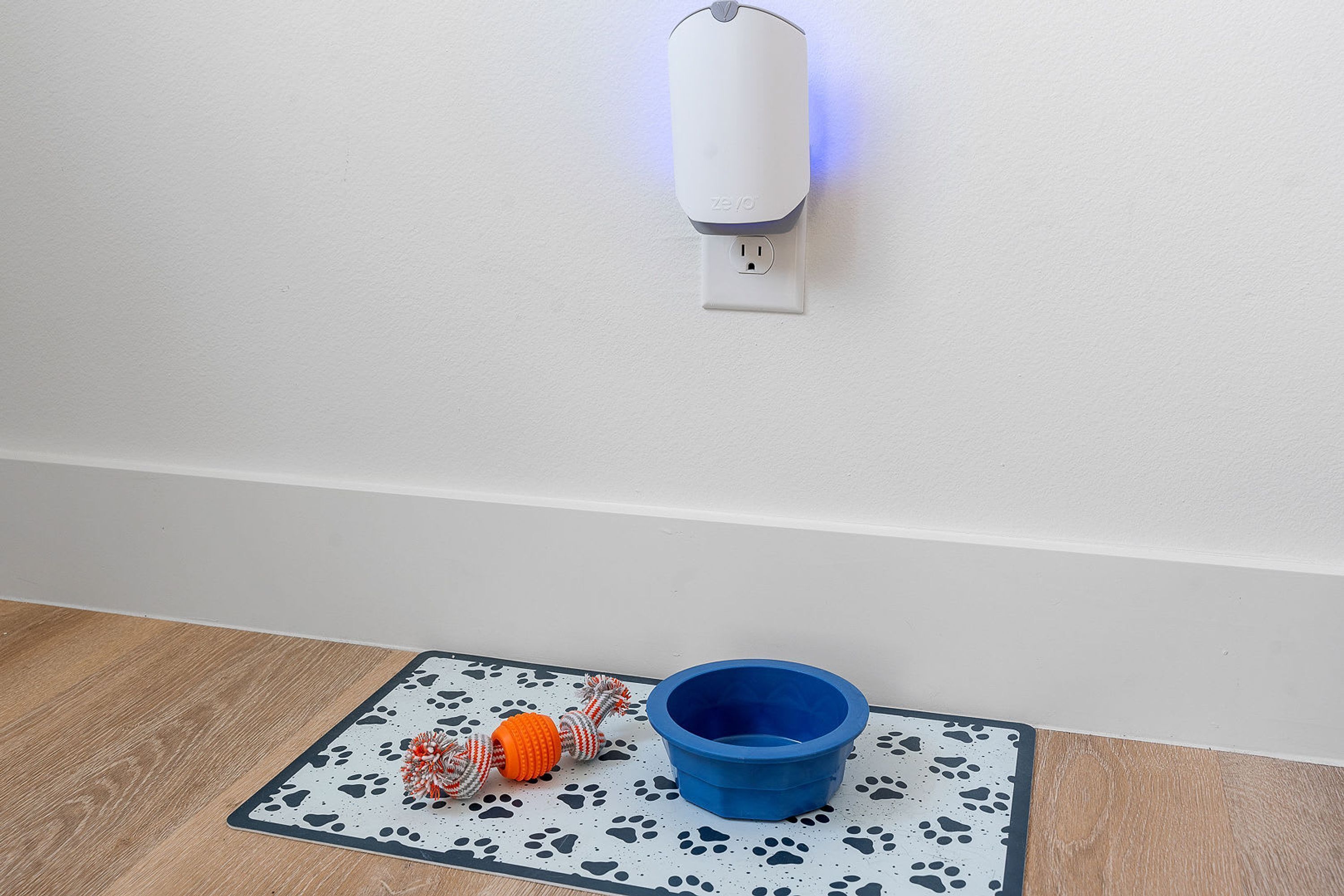 A pet bed with a blue bowl and a toy on a mat.