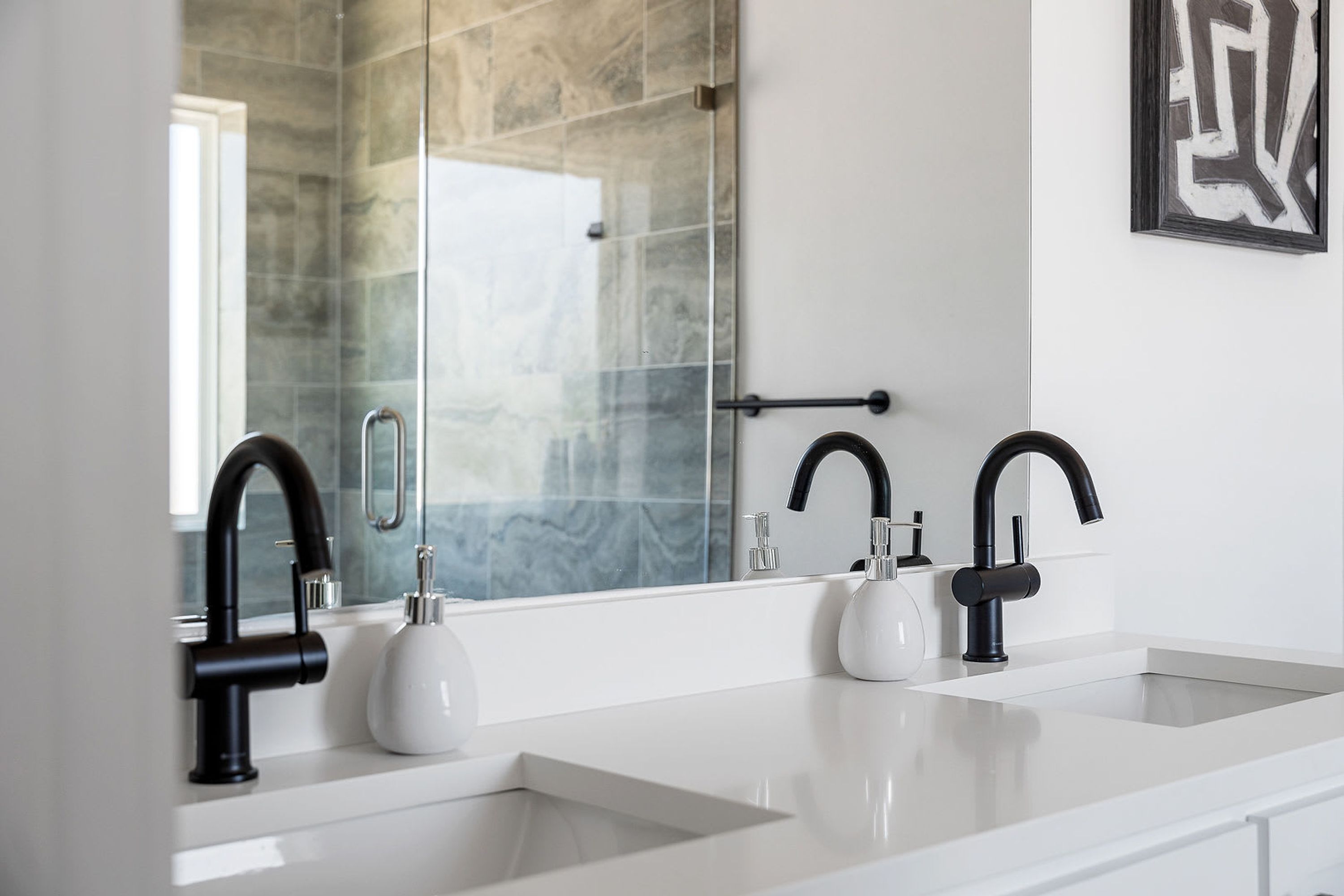 A modern bathroom with two sinks, black faucets, and a large mirror.