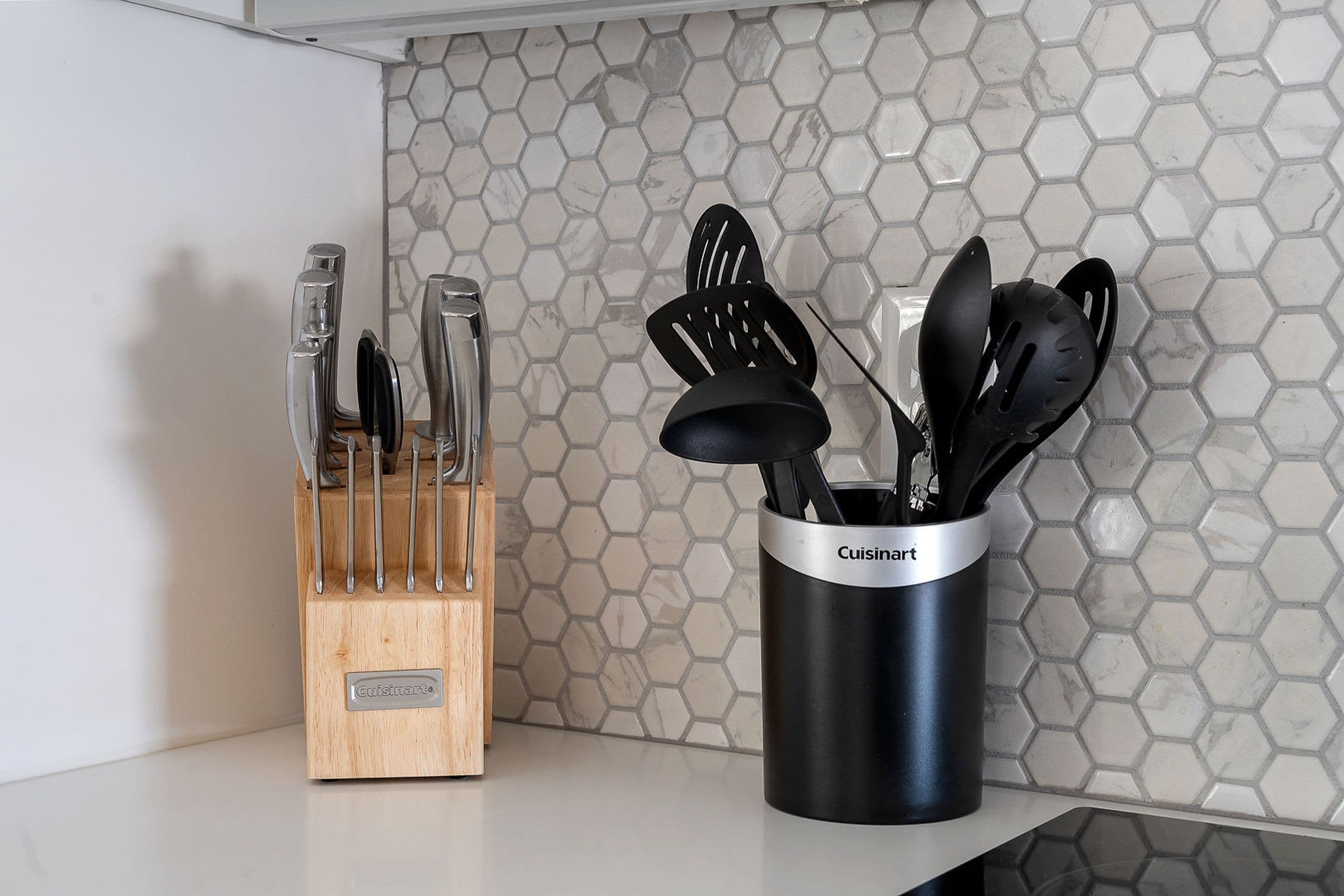 A kitchen counter with a wooden knife block and a black utensil holder labeled "Cuisinart."