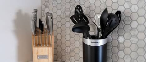A kitchen counter with a wooden knife block and a black utensil holder labeled "Cuisinart."