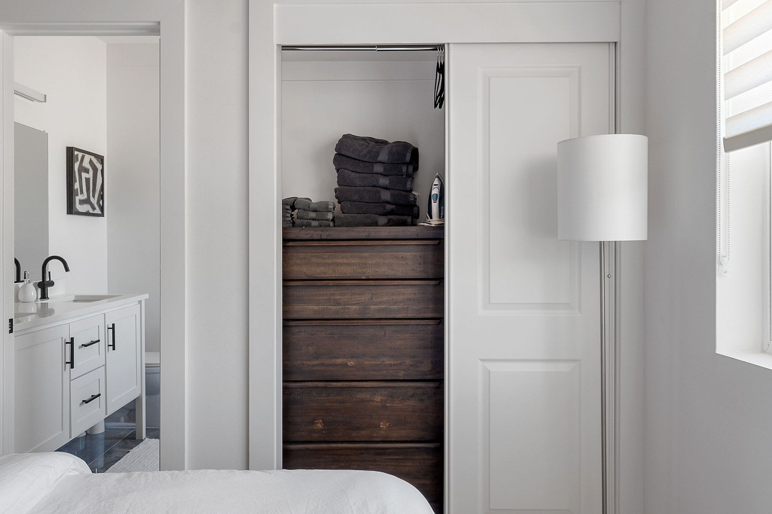 A bedroom with a white bed, a white wardrobe, and a wooden dresser.