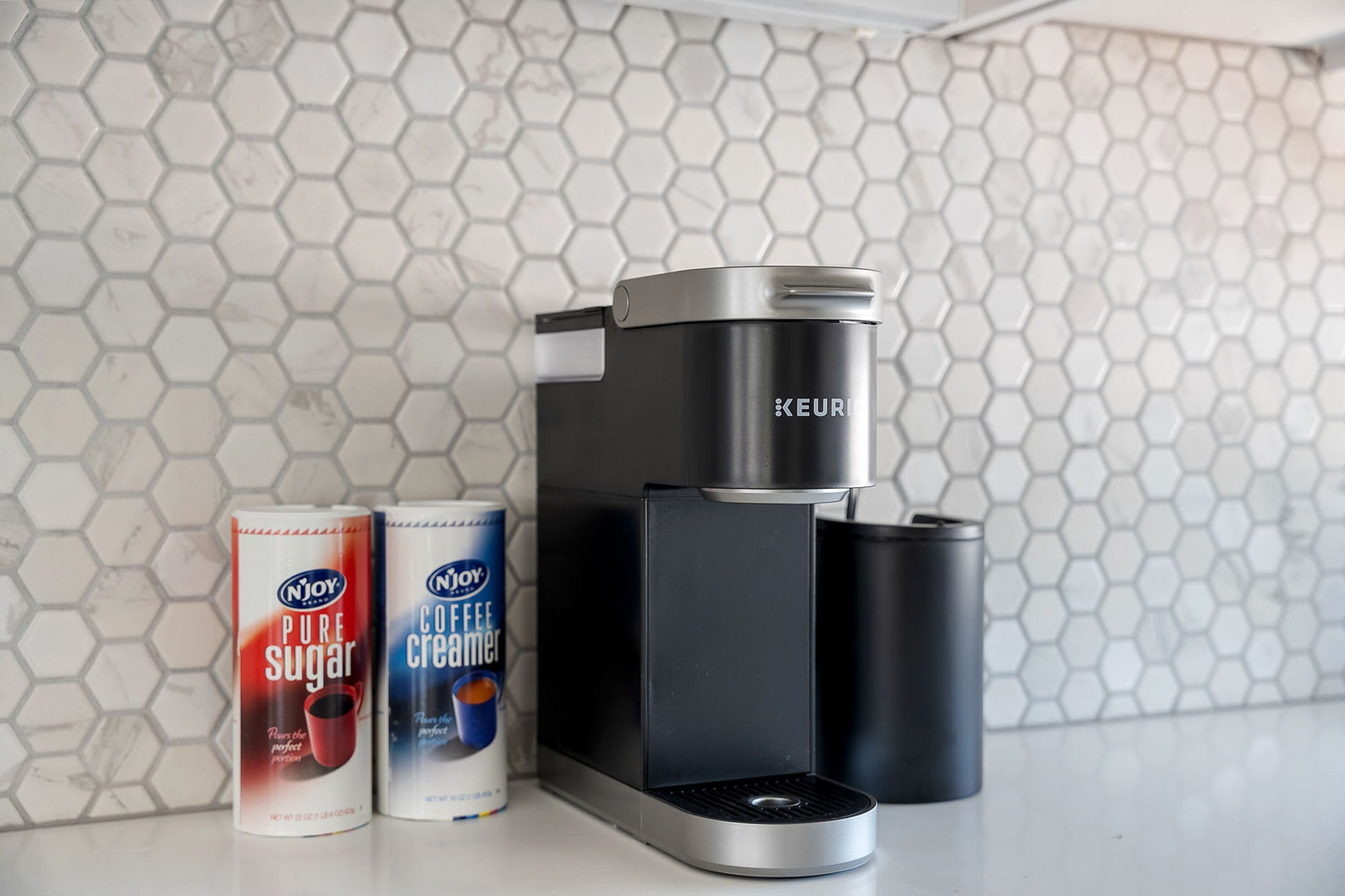 Une machine à café, avec deux boîtes de crème à café Njoy posées à côté.