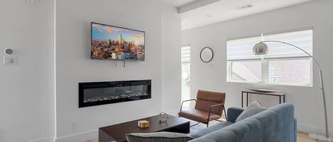 A modern living room with a flat-screen TV, a fireplace, a sofa, a coffee table, and a floor lamp.