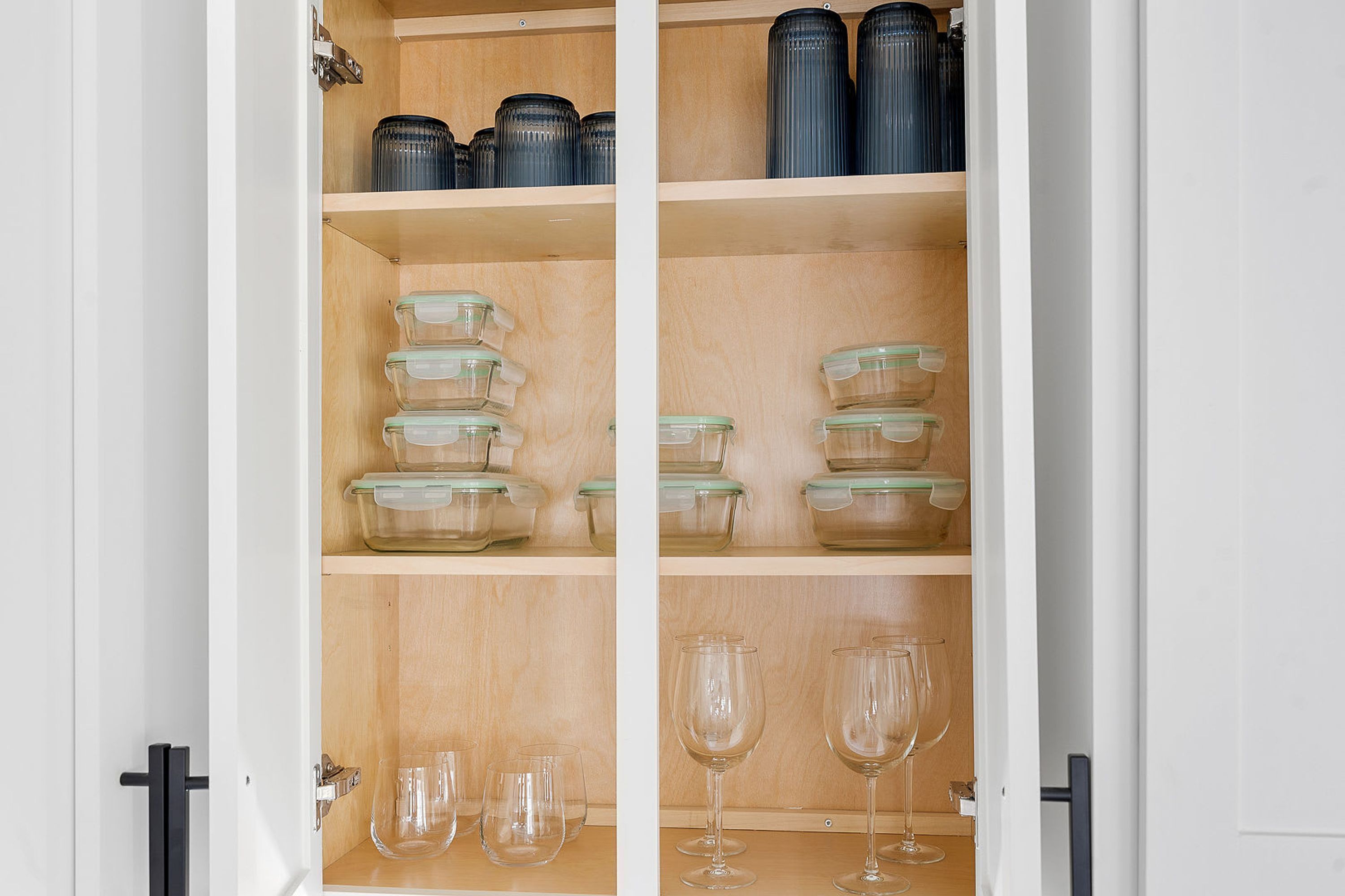 A kitchen cabinet with glass storage containers and wine glasses.
