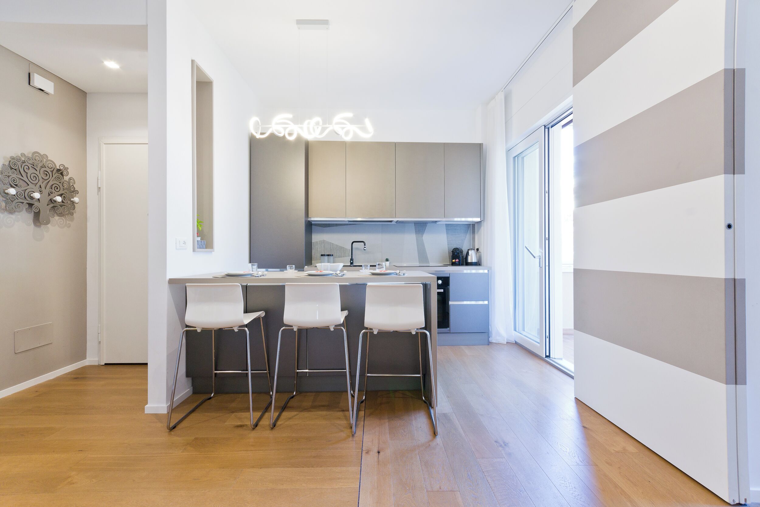 Una cocina moderna con una isla central, taburetes de bar y un elemento decorativo en la pared.