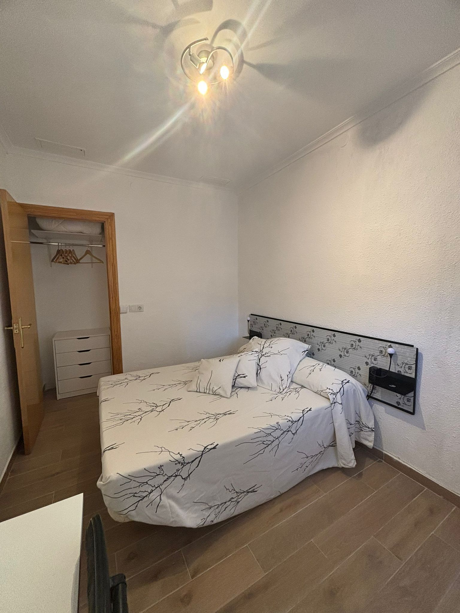 A bedroom with a bed, a bedside table, a hanging light fixture, and a wardrobe.