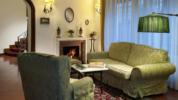 A living room with a fireplace, green patterned sofa, armchairs, and a red patterned rug. - Hotel La Villarosa (Ischia)