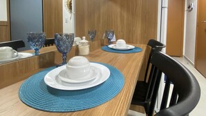 A dining area with a wooden table, blue placemats, white plates, and blue glassware. - Villas do Porto - 307 by La Playa (Ipojuca)