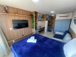 Een kleine hotelkamer met een bed, een televisie, een kitchenette en een kledingkast.