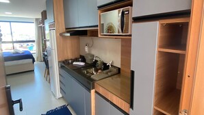 A modern kitchen with grey cabinets, a black countertop, and a built-in oven. There is a blue rug on the floor and a view of the outside through a window. - Villas do Porto - 307 by La Playa (Ipojuca)