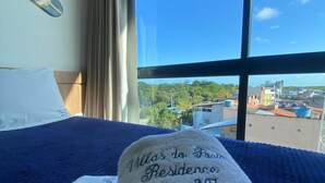 A hotel room with a bed, a window with a city view, and a towel with text. - Villas do Porto - 307 by La Playa (Ipojuca)