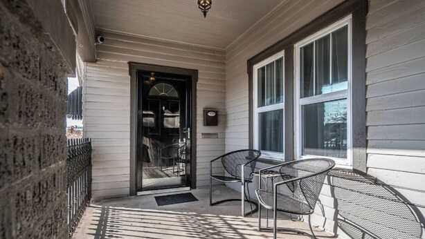 A covered porch with a glass door leading to an interior space, metal chairs, and a small table. - Yellow Stone Western Themed Retreat! By Fairgrounds & Downtown OKC - WiFi! (Oklahoma City)