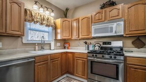 A kitchen with wooden cabinets, a stainless steel dishwasher, a microwave, and a stove. - Yellow Stone Western Themed Retreat! By Fairgrounds & Downtown OKC - WiFi! (Oklahoma City)