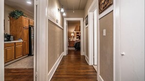 A narrow hallway with wooden cabinets and a refrigerator on the left, leading to a bedroom with a bed and nightstand. - Yellow Stone Western Themed Retreat! By Fairgrounds & Downtown OKC - WiFi! (Oklahoma City)