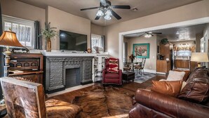 A living room with a fireplace, leather furniture, a television, and a ceiling fan. - Yellow Stone Western Themed Retreat! By Fairgrounds & Downtown OKC - WiFi! (Oklahoma City)