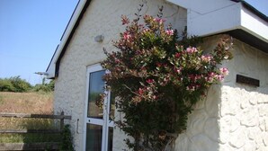 Un bâtiment en pierre avec une porte blanche et une fenêtre, entouré d’une allée gravillonnée et d’une clôture en bois.