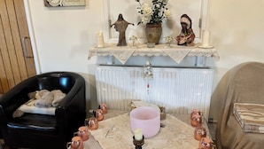Un salon chaleureux avec une cheminée, un fauteuil en cuir noir, une table agrémentée d’objets décoratifs et un radiateur.
