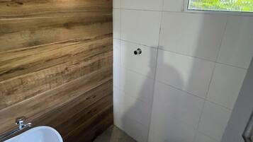 A small bathroom with a wooden wall, a white sink, a toilet, and a window with a view of greenery.