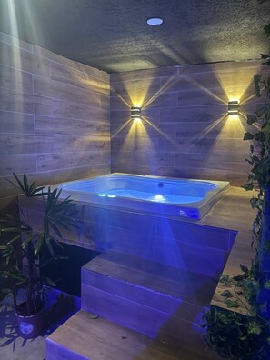 Ein Whirlpool mit Holzverkleidung und Stufen, umgeben von Topfpflanzen und einer strukturierten Wand.