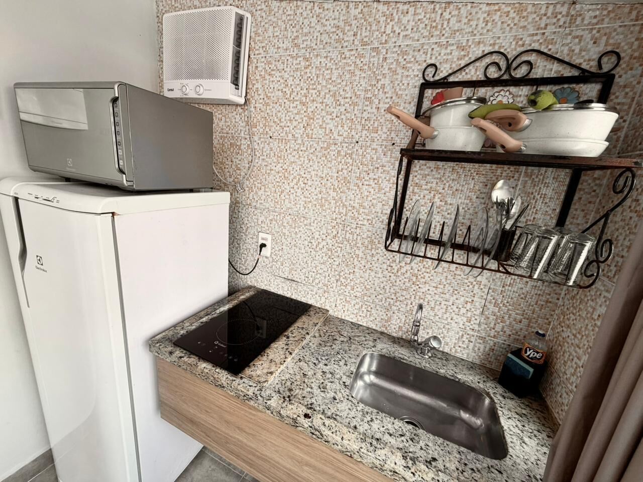 Una cucina compatta con forno a microonde integrato, lavello con piano in granito e porta utensili a parete.