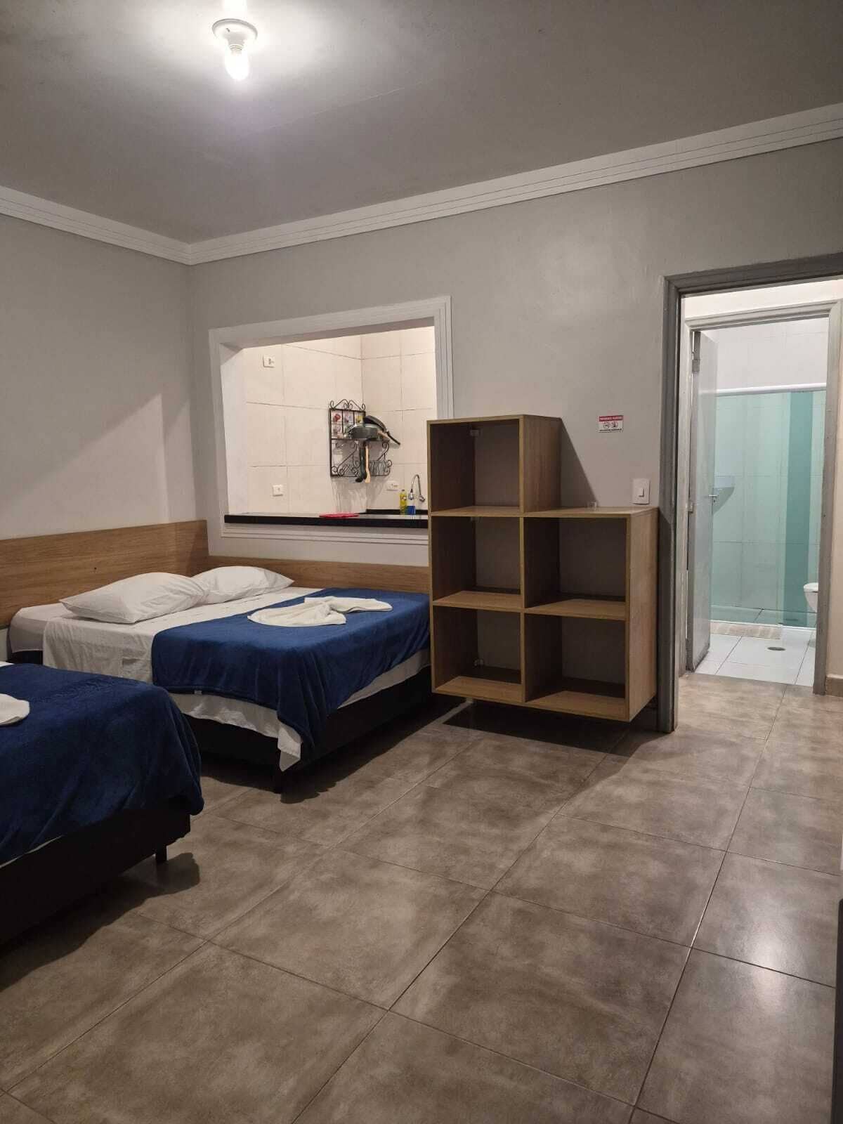 Une chambre d’hôtel avec deux lits, une fenêtre donnant sur un paysage agréable, une étagère en bois et une salle de bain visible à travers une porte ouverte.