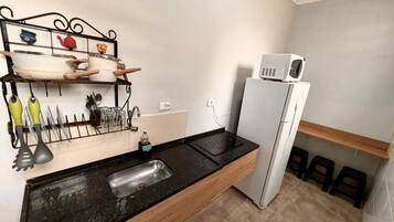 A compact kitchen with a black countertop, a sink, a white refrigerator, and a shelf with kitchen utensils.