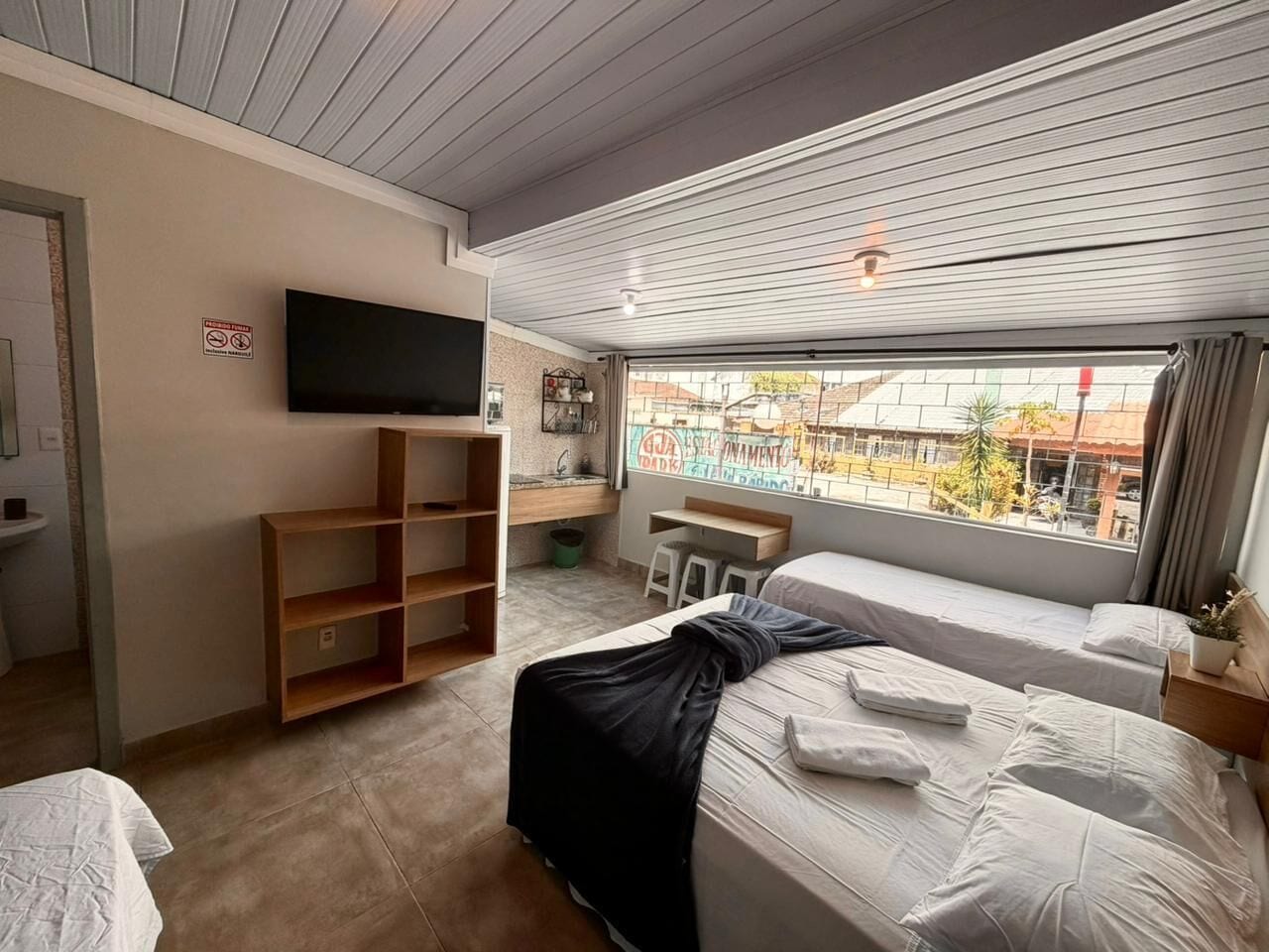 Une chambre d’hôtel équipée d’un lit, d’un bureau, d’une télévision et d’une fenêtre donnant sur l’extérieur.