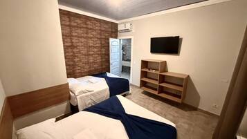 A hotel room with two beds, a brick accent wall, a TV, and a wooden shelf.