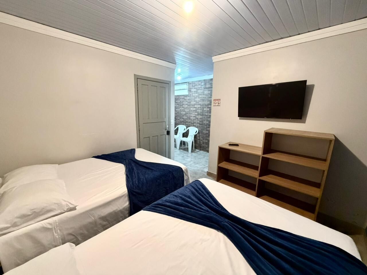 A room with two beds, a TV mounted on the wall, and a wooden shelf unit.