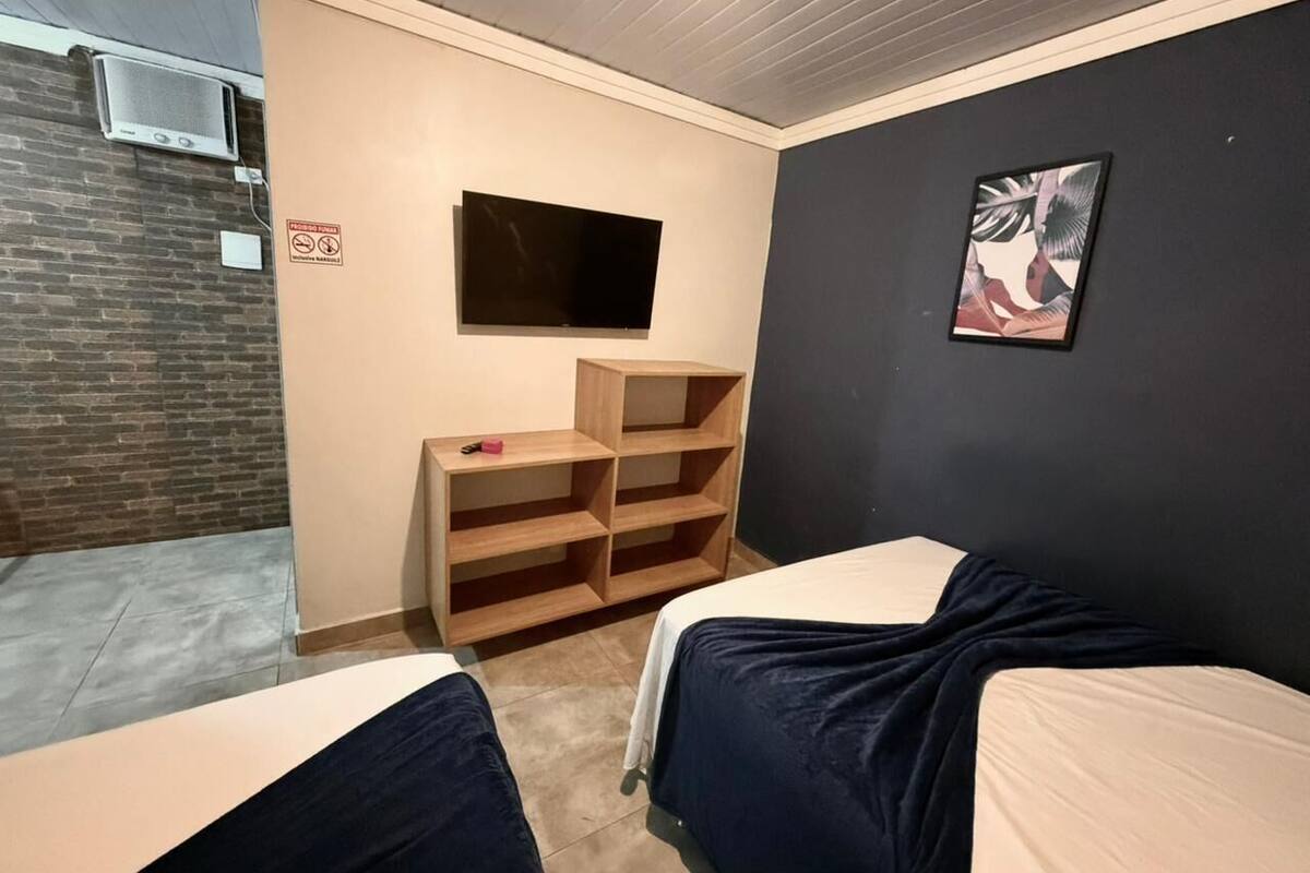 Une chambre avec deux lits, une télévision, une bibliothèque et un tableau au mur.