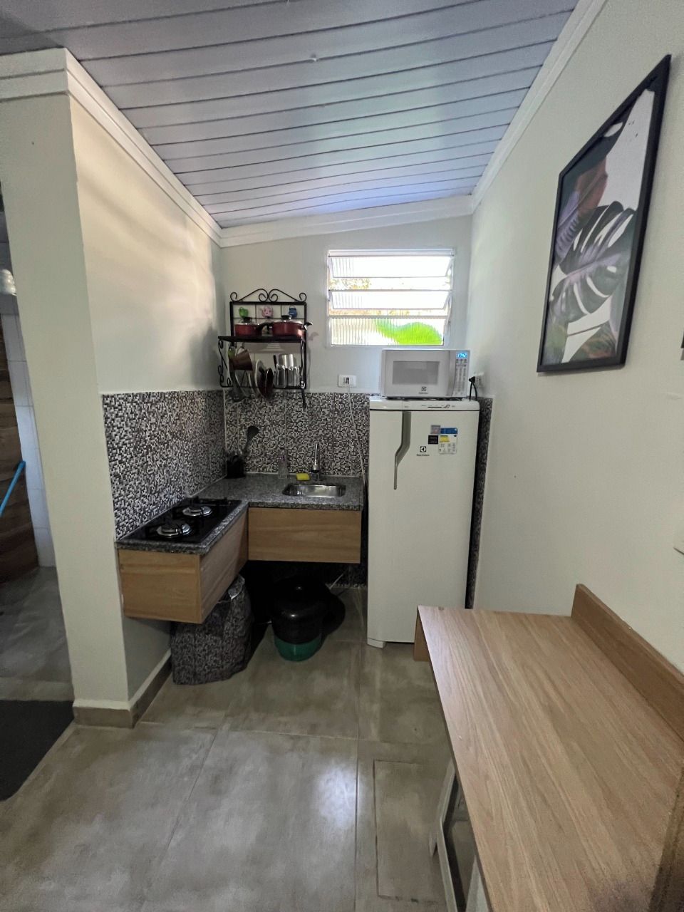 A compact kitchen with a microwave, sink, and stove. There's a window providing natural light and a small refrigerator.