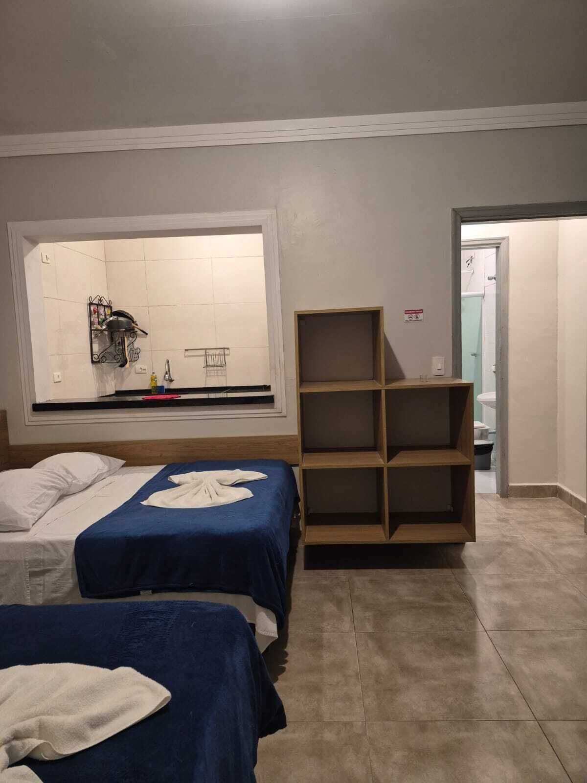 Habitación de hotel con dos camas, un ventanal grande, un estante de madera y vista al baño.