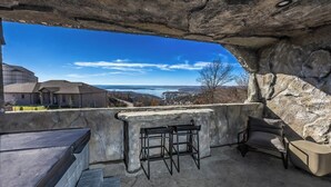 An outdoor seating area with stone walls and a view of a body of water and buildings in the distance.