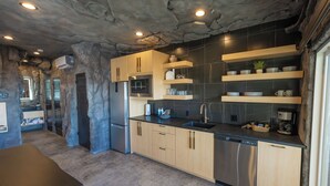 A modern kitchen with wooden cabinets, a stainless steel refrigerator, a dishwasher, and black tiled backsplash.