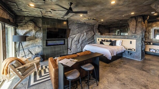 A modern room with a stone wall, a bed, a desk, and a ceiling fan.
