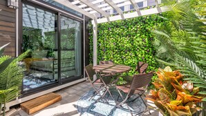 Un patio con puerta de cristal, una mesa y sillas, y una pared cubierta de follaje verde.