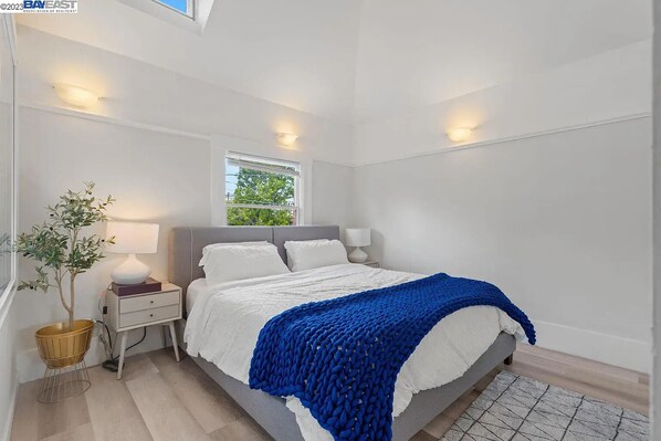 Un dormitorio con una cama, lámparas de noche, una mesita de noche, una planta en maceta y una ventana.