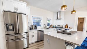 Una cocina moderna con electrodomésticos de acero inoxidable, una isla central e iluminación colgante.