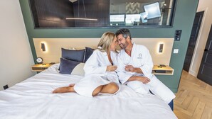 A modern hotel room with a large bed, bedside tables, and a view of the city through a large window. - Luxury Treehouse Retreat with Private Hot Tub (Branson)