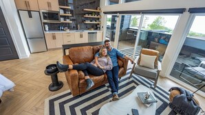 A modern living room with a sofa, a coffee table, and a dining area with a kitchen in the background. - Luxury Treehouse Retreat with Private Hot Tub (Branson)