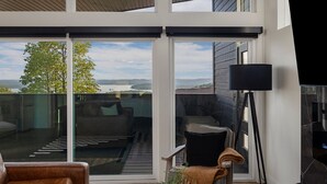 A modern living room with a large sliding glass door leading to an outdoor deck, a black floor lamp, and a cozy seating area with a brown leather chair and a small table.