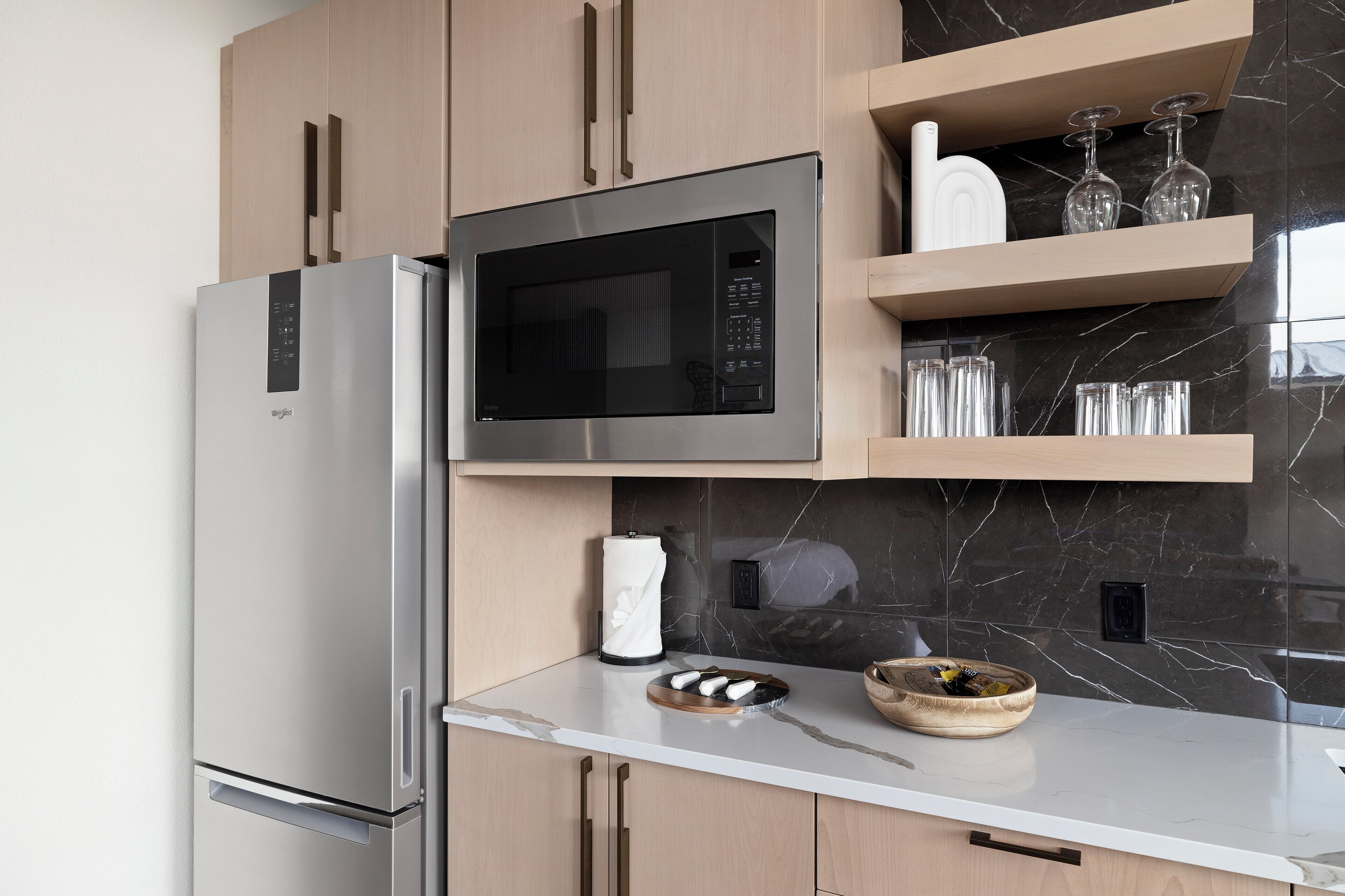 A modern kitchen with a built-in microwave, stainless steel refrigerator, and marble backsplash.
