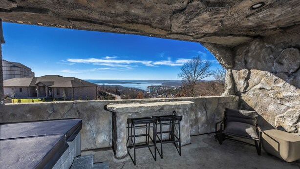 A stone-enclosed outdoor seating area with a view of a lake and distant buildings.