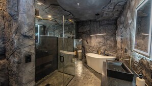 A modern bathroom with a stone wall design, a glass shower enclosure, a freestanding bathtub, and a black vanity with a sink.