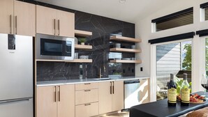 Eine moderne Küche mit eingebauter Mikrowelle, Edelstahlgeräten und Holzausbau. Ein Essbereich mit Tisch für zwei Personen und ein Fenster mit Blick ins Freie.